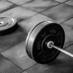Grayscale image of heavy gym barbell and weights on rubber mat flooring.